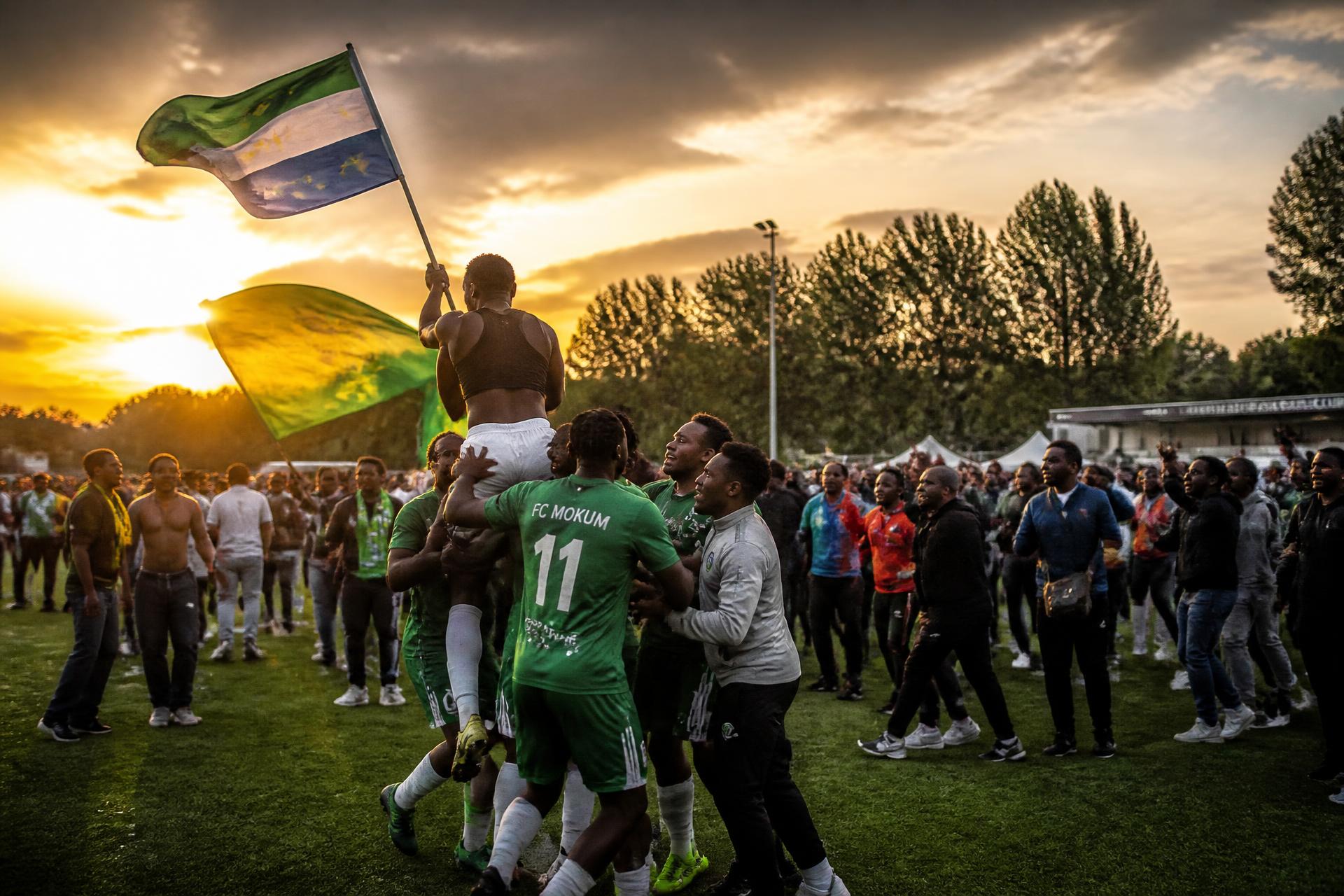 AFCOH players and supporters celebrating on the pitch at sunset